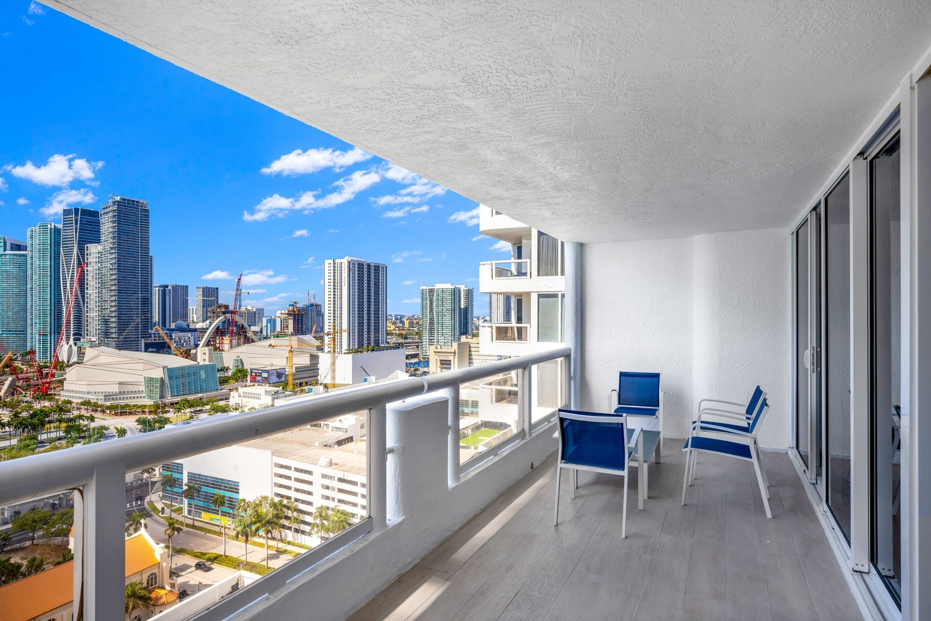 Un balcón con vista a la ciudad, paredes blancas y dos sillas azules.