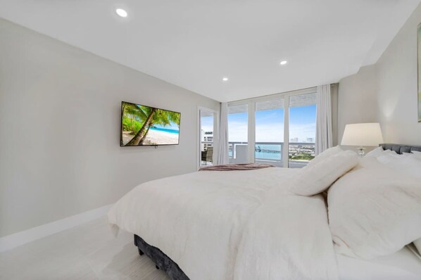 A bedroom with a large bed, a TV mounted on the wall, and a view of the beach through the window. - City Vibes Ocean View Next to Art Basel (Miami)
