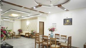 A dining area with wooden furniture, a ceiling fan, and a wall-mounted painting. - Purple Tree Villa Delhi  (New Delhi)