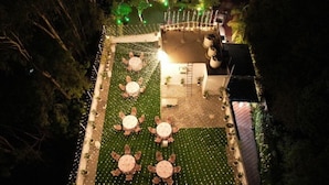 An outdoor dining area with round tables and chairs, surrounded by greenery and string lights. - Purple Tree Villa Delhi  (New Delhi)