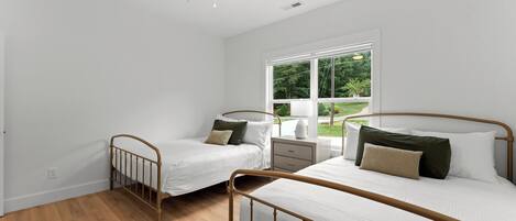 Een slaapkamer met twee eenpersoonsbedden, een nachtkastje, een raam met uitzicht op groen, en een wit plafond.