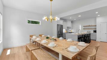 Una cocina moderna con armarios blancos, un refrigerador de acero inoxidable y una mesa de comedor de madera para seis personas.