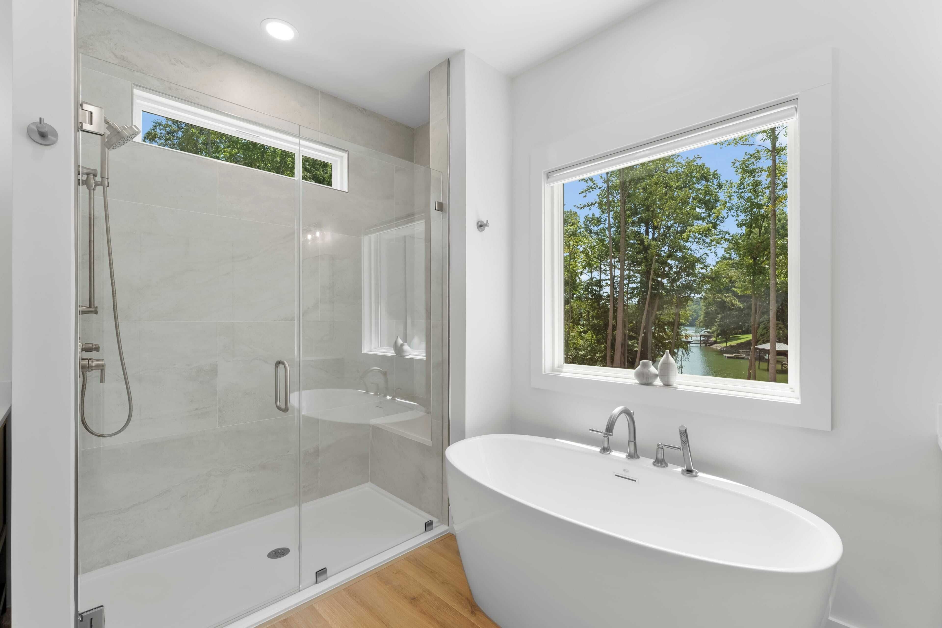 Une salle de bain moderne dotée d’une douche à parois de verre, d’une baignoire sur pieds et d’une fenêtre donnant sur la verdure.