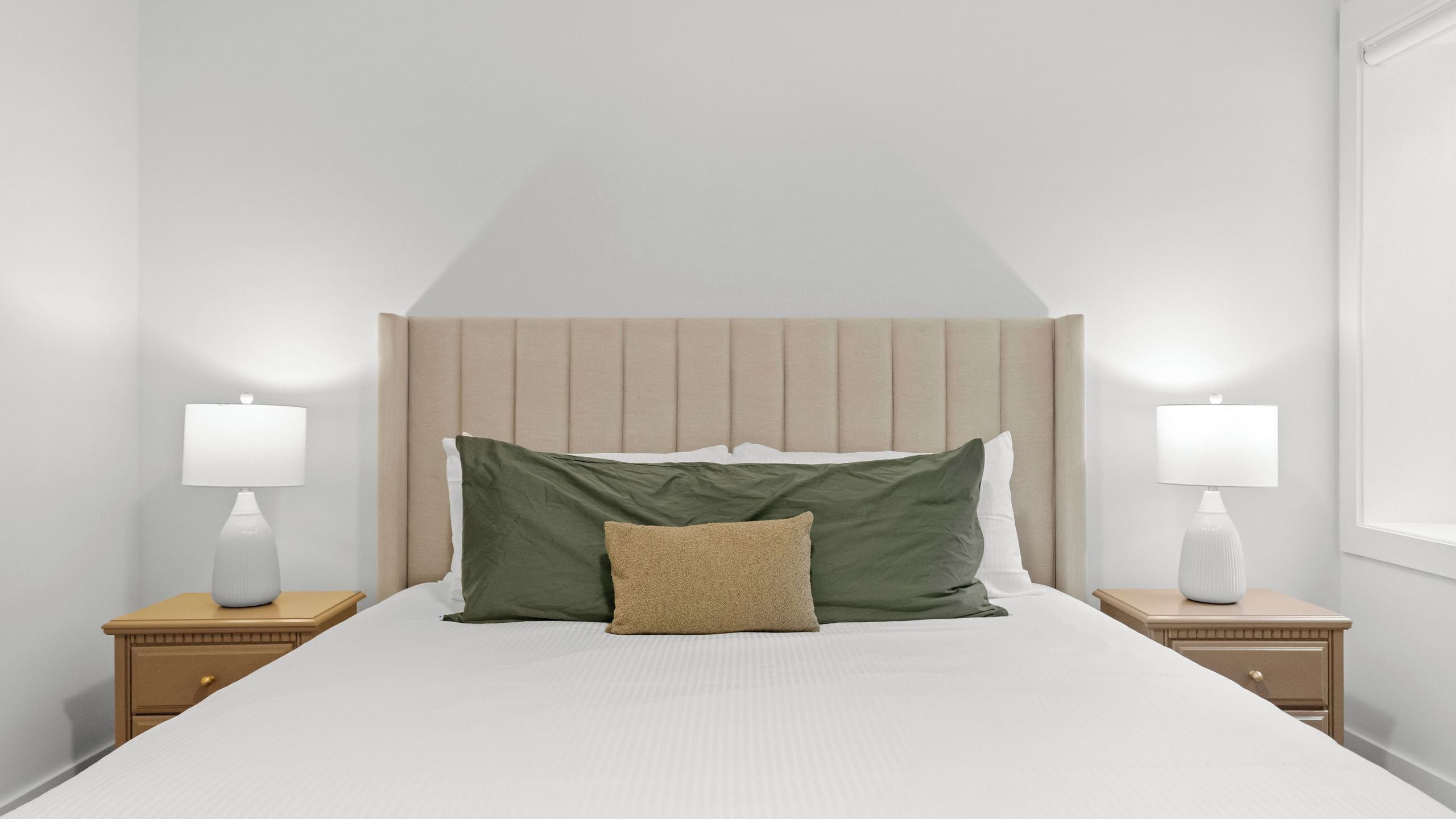 Un dormitorio ordenado con una cama grande, dos mesitas de noche y un cabecero.