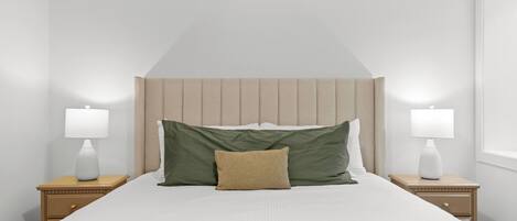 Un dormitorio ordenado con una cama grande, dos mesitas de noche y un cabecero.