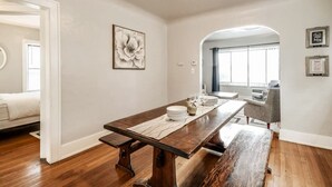 Een eetgedeelte met een houten tafel gedekt voor vier personen, witte wanden en een groot schilderij van bloemen.