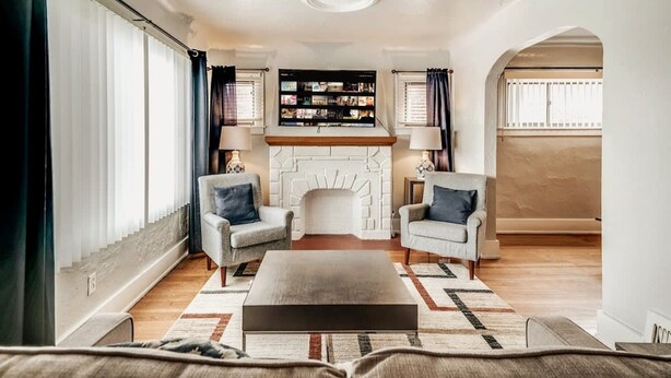 Een woonkamer met een open haard, twee fauteuils, een salontafel en een televisie boven de haard.