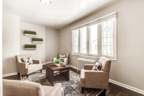 A living room with two sofas, a coffee table, and a radiator. There are three wall-mounted planters with green plants. - Great 6 Bedroom Peaceful Family Retreat in the University District (Detroit)