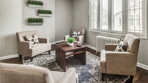 Ein Wohnzimmer mit zwei Sesseln, einem Couchtisch und einem großen Fenster mit Blick auf ein Gebäude.