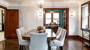 Comedor con una mesa de madera y seis sillas tapizadas, una araña y vista a otra zona de comedor a través de un vano.