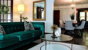 Una sala de estar con un sofá verde, una mesa de centro de vidrio, una lámpara y un espejo en la pared.