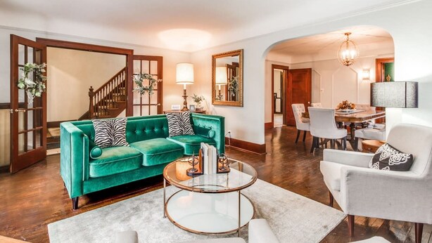 Una sala de estar con un sofá verde, una mesa de centro de vidrio y un comedor con sillas blancas.