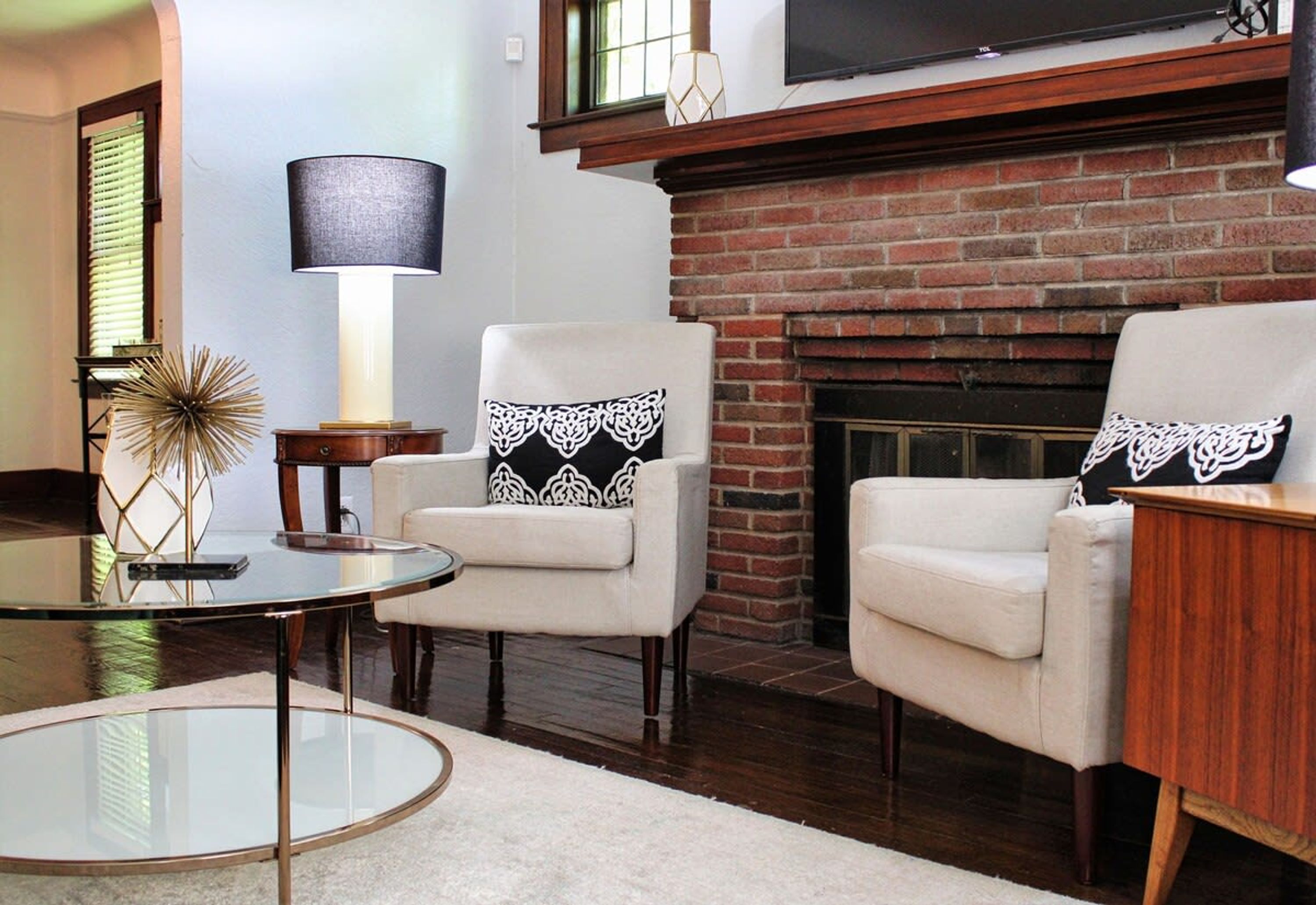 A living room with two armchairs, a round glass coffee table, a lamp, and a fireplace.
