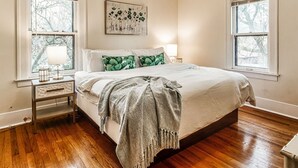 Un dormitorio con una cama grande, dos mesitas de noche, una mesita auxiliar, un ventanal con vistas y una obra de arte colgada en la pared.