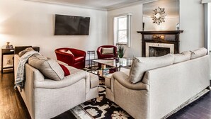 A living room with a fireplace, a television, and a red chair. - Spacious Luxury Home 5 min to Detroit Golf Club 4 car Free Parking (Detroit)