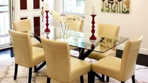 A dining area with a glass table surrounded by four beige chairs, a vase with white flowers, and red candle holders. - Spacious Luxury Home 5 min to Detroit Golf Club 4 car Free Parking (Detroit)