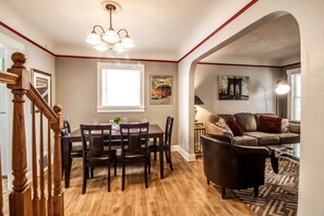 A dining area with a wooden table and chairs, a chandelier, and a large window. - Automaniac Spot in the Heart of Pontiac 3 Beds 2 Baths (Pontiac)