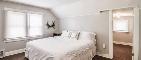 Une chambre avec un grand lit, des murs blancs, un luminaire au plafond et une fenêtre avec des stores.