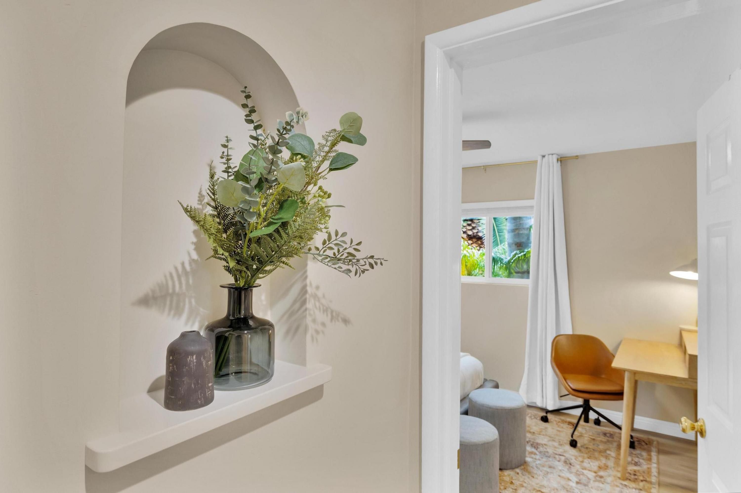 A modern room with a white wall, a shelf with a vase of greenery, a desk with a chair, and a window with curtains.