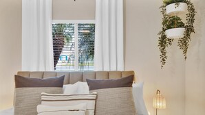 A neatly made bed with multiple pillows, a bedside lamp, and a hanging plant. - Designer Coastal Paradise w Pool - Steps to Beach (Carlsbad)
