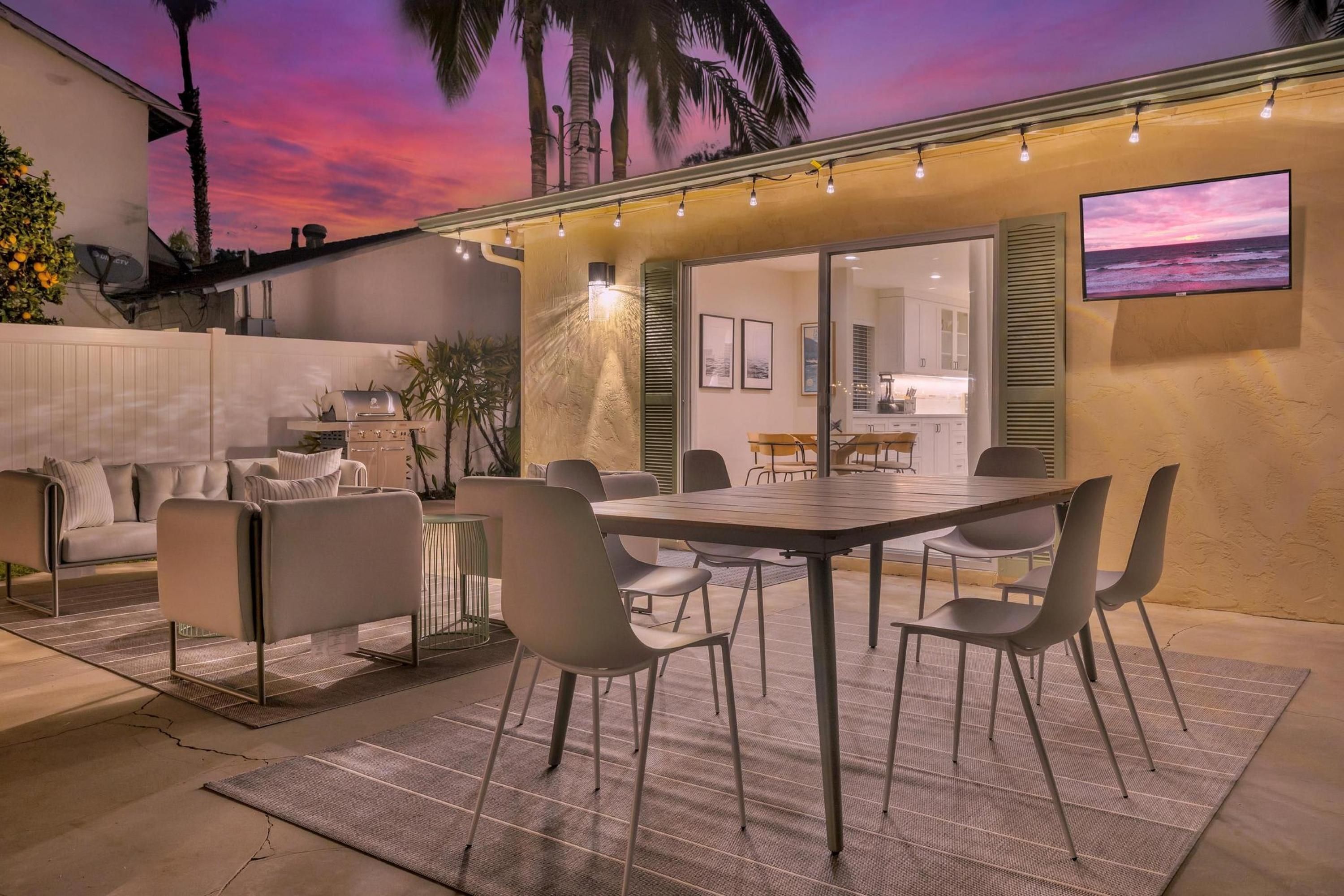 An outdoor dining area with a table and chairs, a grill, and a TV mounted on the wall.