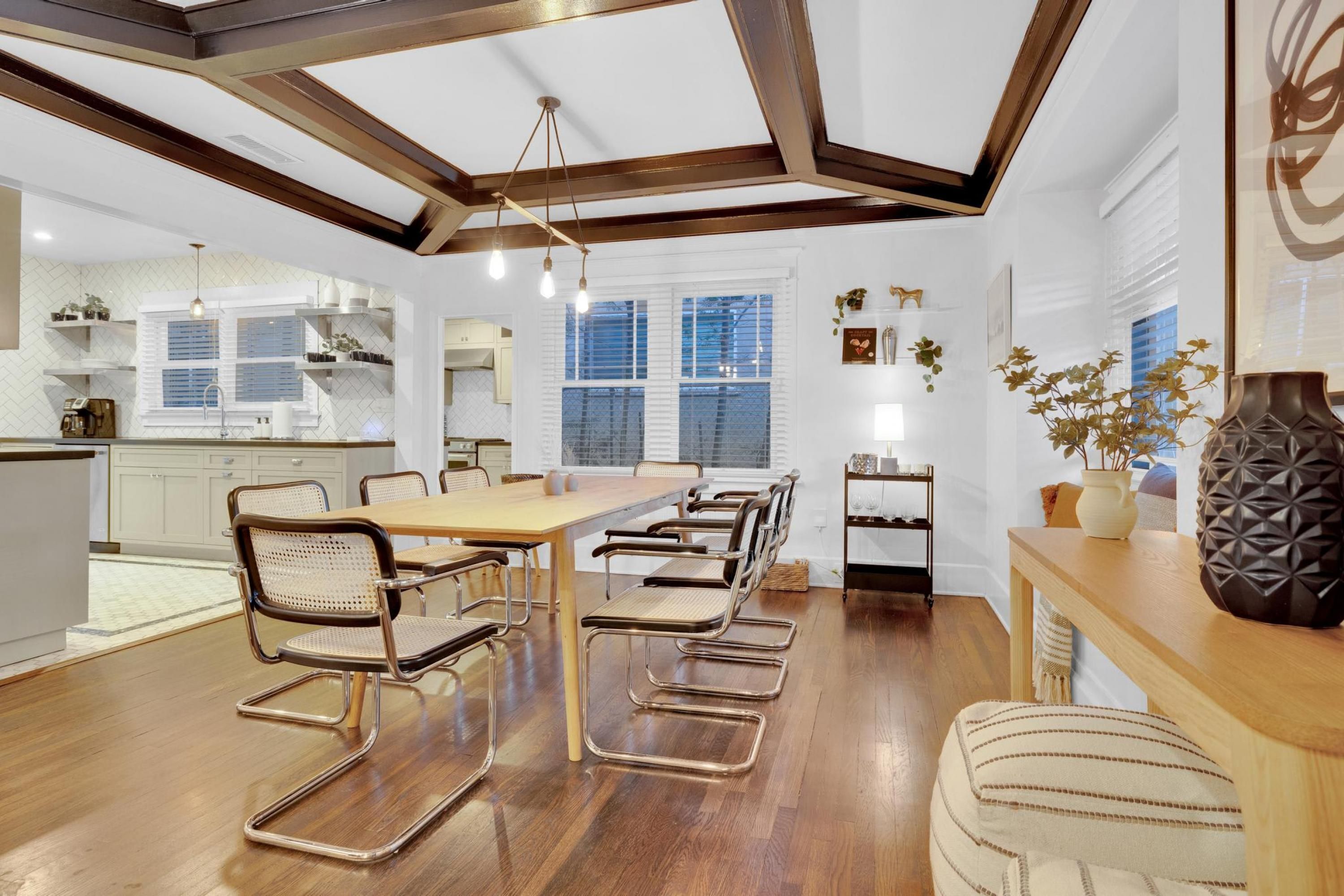 Uma cozinha moderna com uma mesa e cadeiras de madeira, uma área de refeições com janela e um vaso decorativo sobre uma mesa lateral.