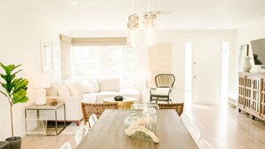 A modern dining area with a wooden table, white chairs, and hanging light fixtures. - Stunning Beach Hideaway w Luxury Outdoor Living (San Diego)