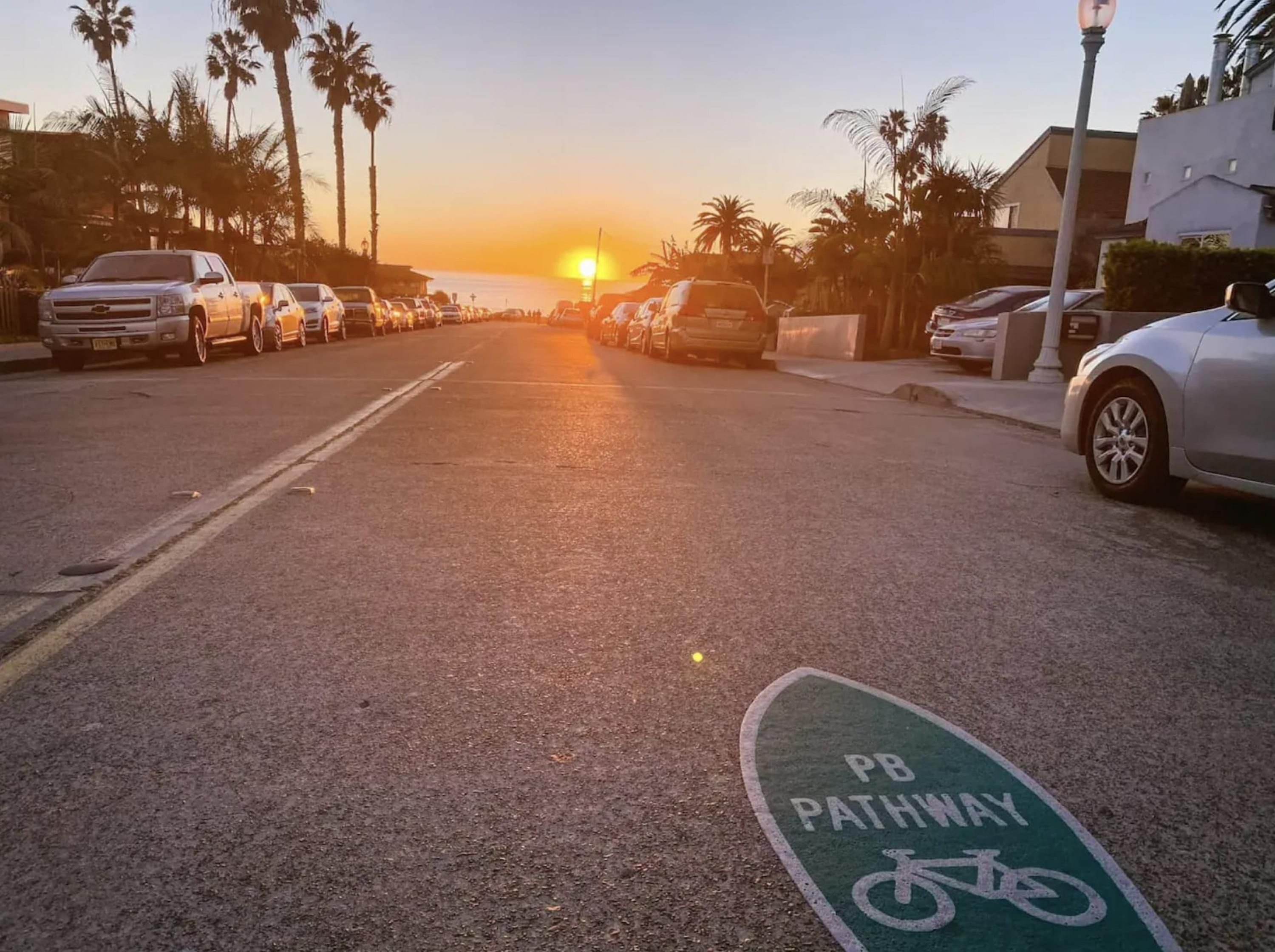 A street with parked cars and a bike path marked with "PB PATHWAY" and a bicycle symbol.