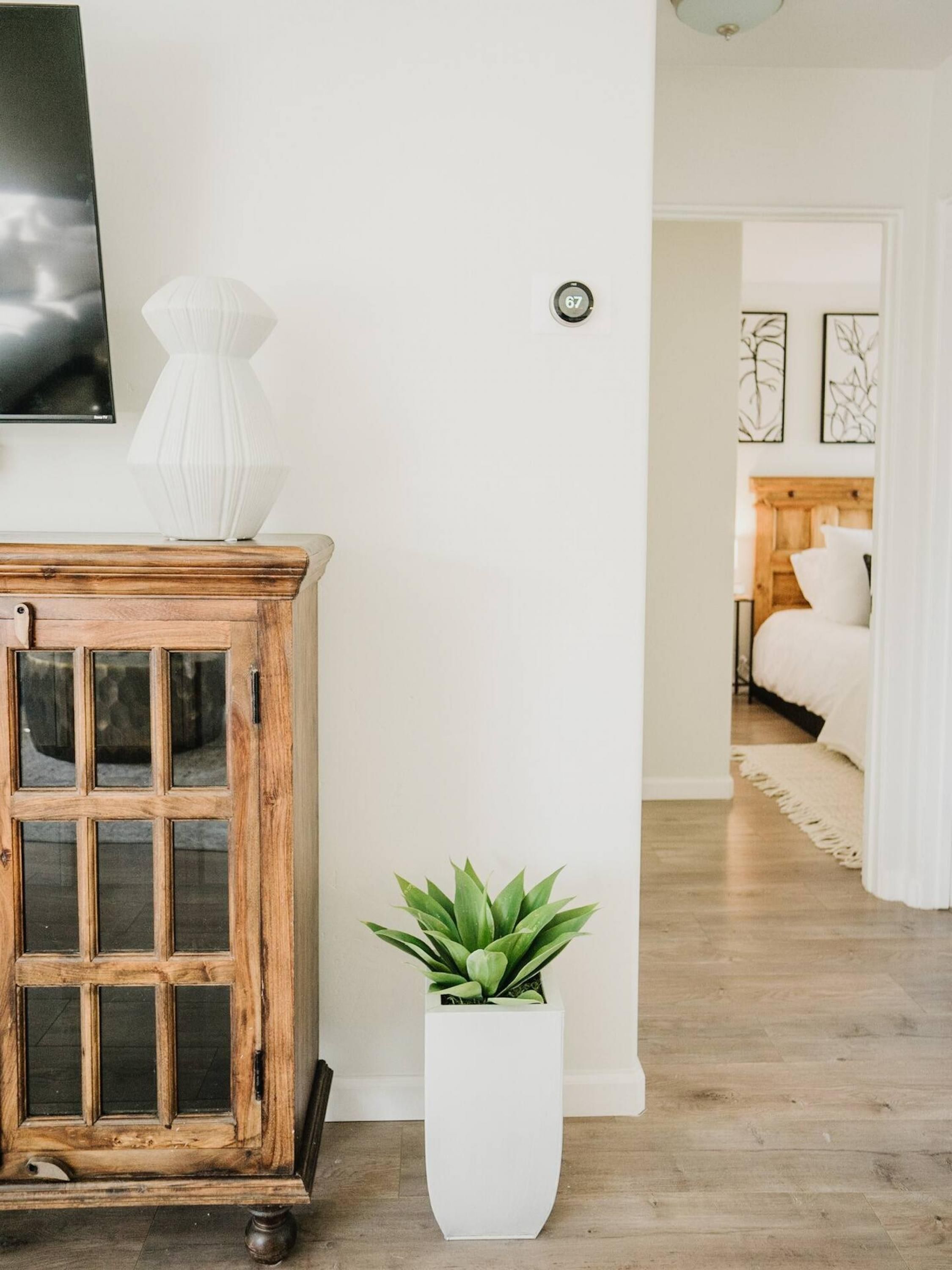 Una sala de estar con un aparador de madera, una planta en maceta y una cama al fondo.