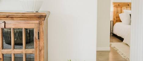 Una sala de estar con un aparador de madera, una planta en maceta y una cama al fondo.