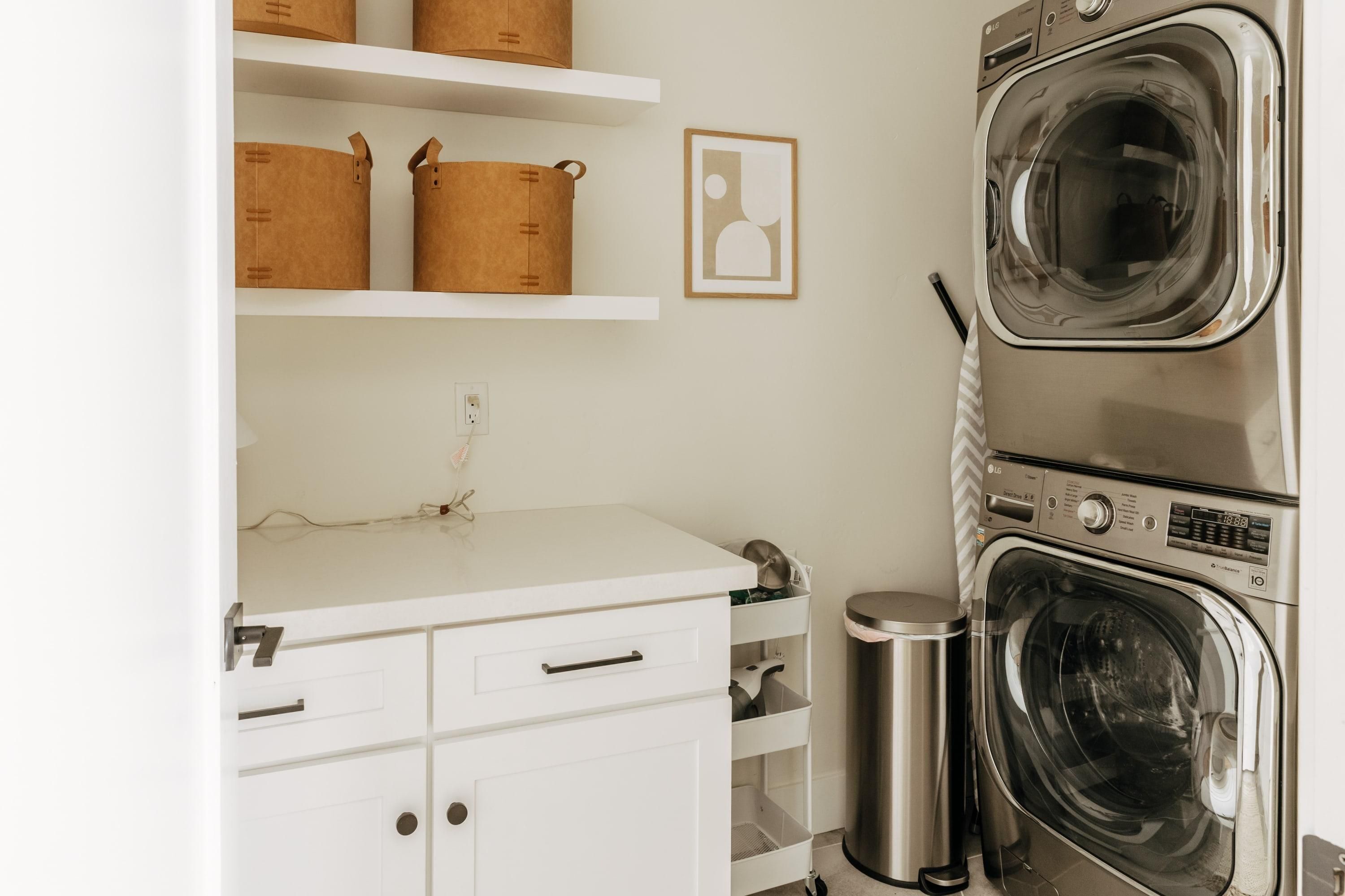 A laundry area with stacked washers and dryers, a white countertop, and storage baskets on shelves.