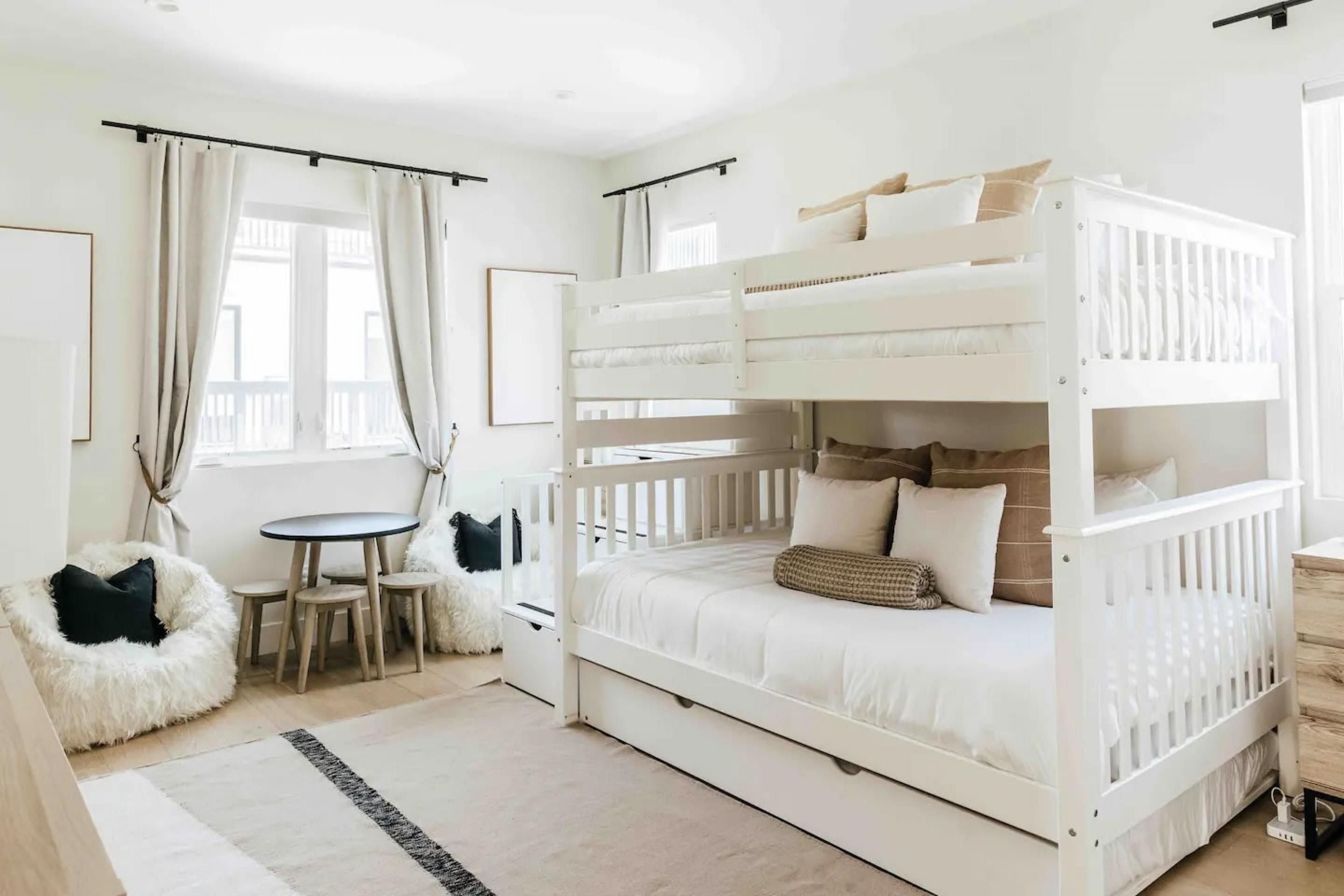 A bunk bed room with a small table and chairs, a fluffy chair, and a view of the outside.