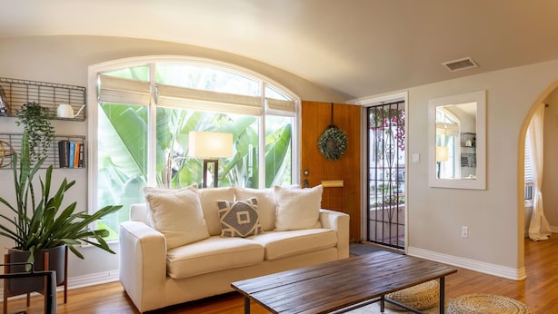 A spacious living room with a white sofa, a wooden coffee table, and a large window with a view of greenery.