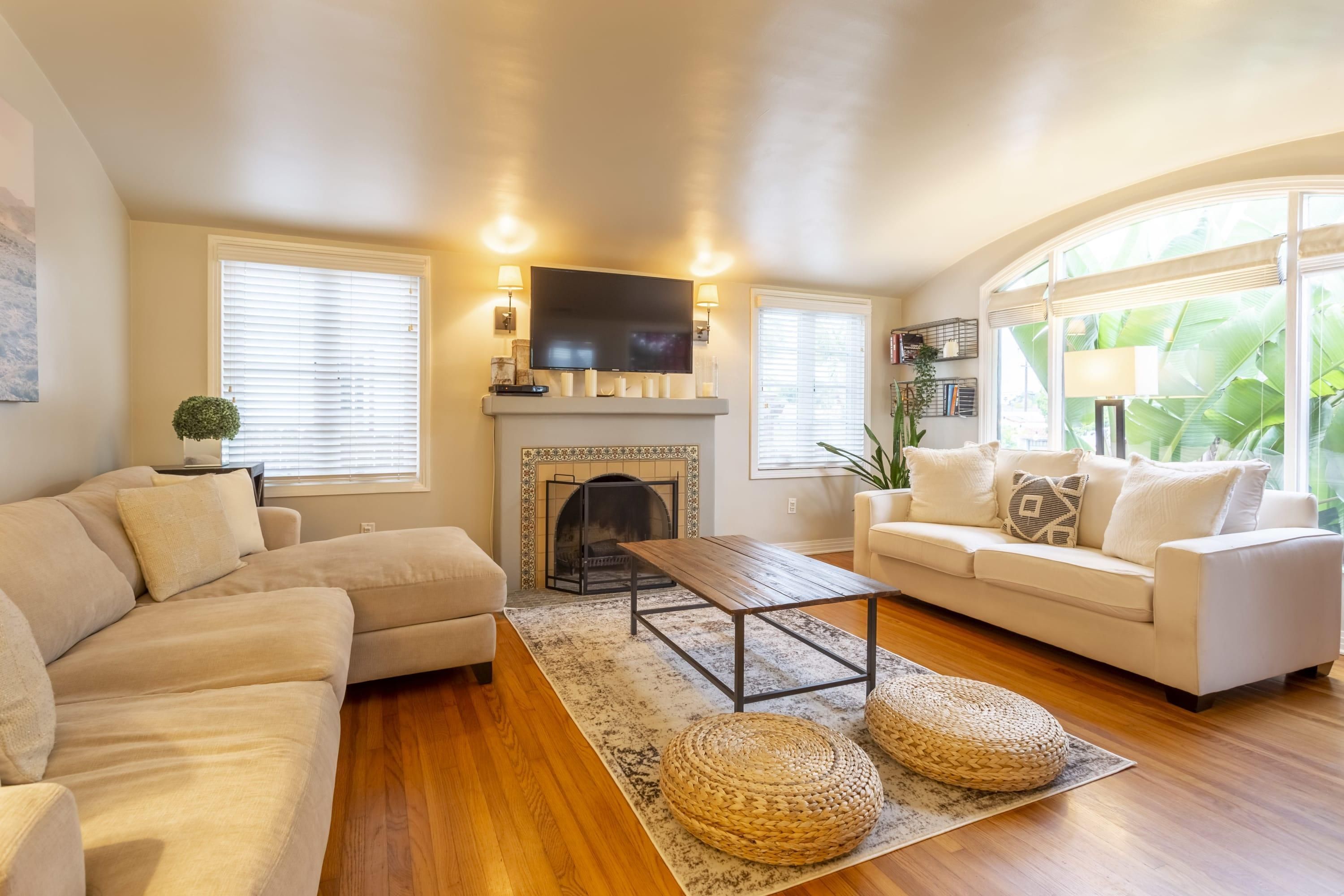 A living room with a fireplace, two sofas, a coffee table, and large windows with blinds.