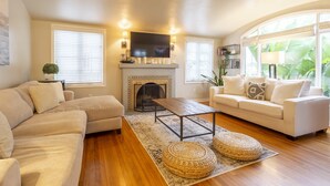 A living room with a fireplace, two sofas, a coffee table, and large windows with blinds.