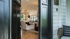 A wooden door leading into a living room with a sofa, a wicker chair, and a chandelier. - Spacious 5 BR Near Heart of South Park (San Diego)