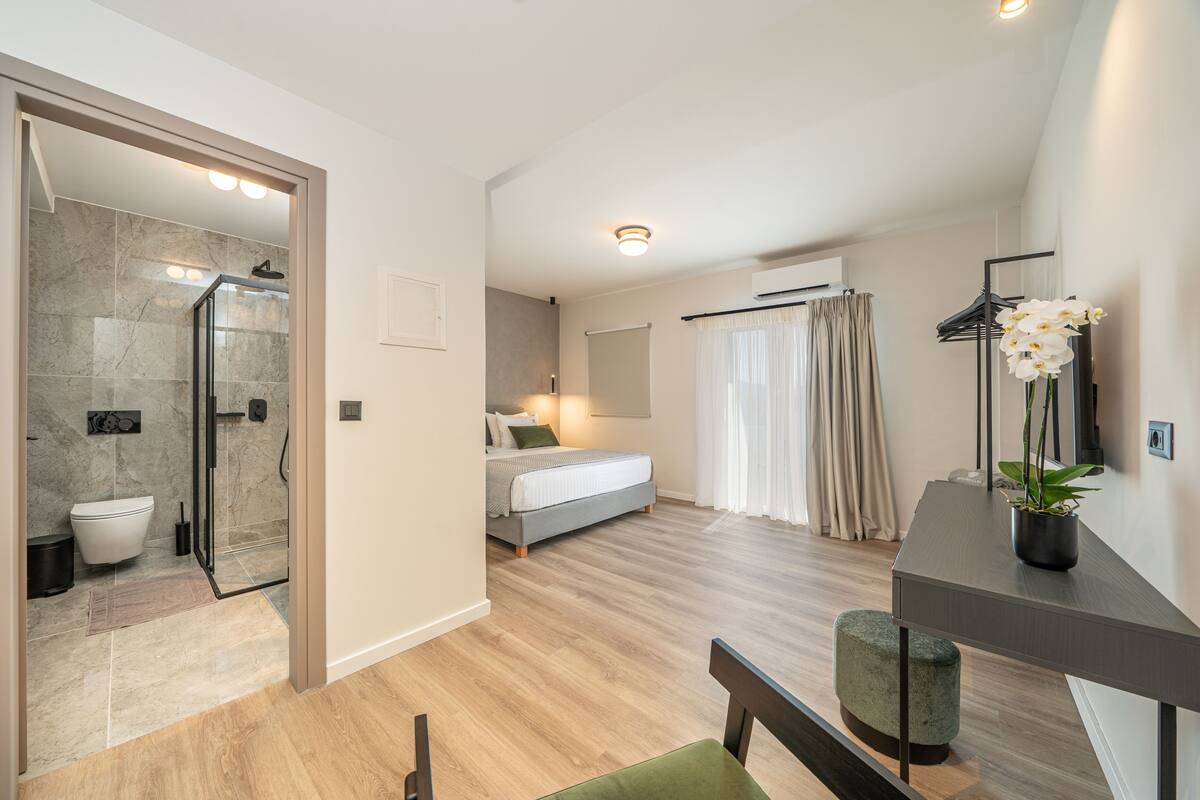 A modern bedroom with a bed, a bedside table, a mirror, and a shower area.