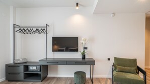 Una habitación moderna con un escritorio gris, un televisor montado en la pared, una silla verde y una pequeña planta en maceta.