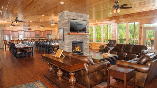 A spacious living area with a stone fireplace, leather furniture, and a large TV mounted on a stone wall. - Greenbrier Estate Luxury Theaters Mesmerizing Views (Sevierville)