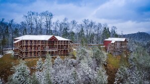 A large wooden cabin with multiple balconies, surrounded by snow-covered trees and a lake. - Greenbrier Estate Luxury Theaters Mesmerizing Views (Sevierville)