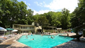 A swimming pool with lounge chairs and umbrellas, surrounded by trees and a building with a balcony. - Skyline Splendor Luxe Retreat With Breathtaking Views Over Downtown Gatlinburg (Gatlinburg)