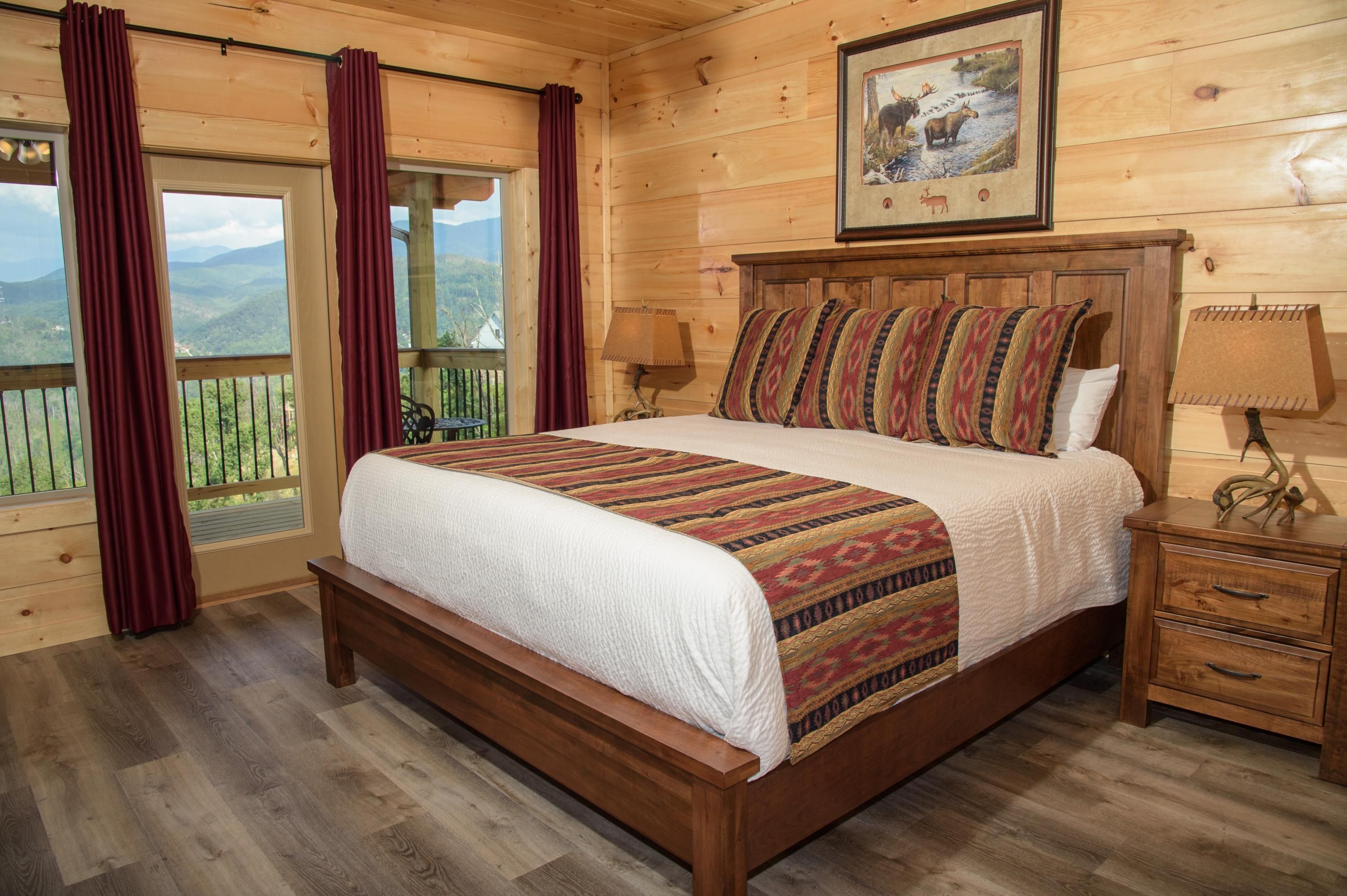 A wooden room with a large bed, a nightstand, and a window with curtains.
