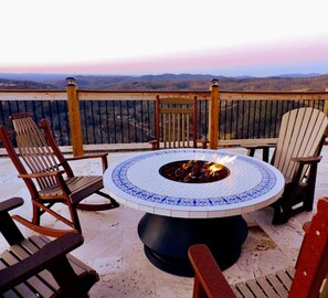 A round outdoor fire pit table with chairs around it, set on a balcony with a view of distant mountains. - Skyline Splendor Luxe Retreat With Breathtaking Views Over Downtown Gatlinburg (Gatlinburg)