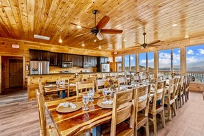 Une cabane en bois comprenant un coin repas, une cuisine et de grandes fenêtres donnant sur un paysage pittoresque.