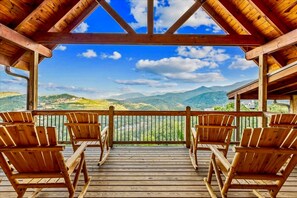 A wooden deck with chairs and a view of mountains. - Skyline Splendor Luxe Retreat With Breathtaking Views Over Downtown Gatlinburg (Gatlinburg)