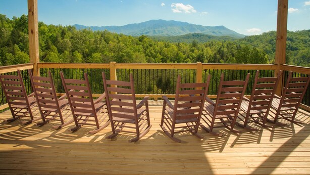 A wooden deck with six rocking chairs facing a forested mountain range. - Breathtaking 14br Cabin Elevator Views Games Hot Tubs Galore (Sevierville)