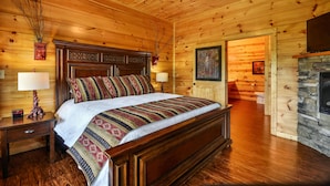 A wooden cabin-style bedroom with a large bed, wooden walls, a stone fireplace, and a ceiling fan. - Breathtaking 14br Cabin Elevator Views Games Hot Tubs Galore (Sevierville)
