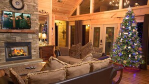 A cozy living room with a fireplace, a television mounted on a stone wall, and a Christmas tree. - Gatlinburg s Finest Majestic Views Home Theater Hot Tubs and More (Gatlinburg)