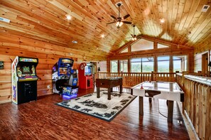 A wooden cabin interior with arcade games, a foosball table, and large windows offering a view of the outdoors. - Luxury 14br Haven Views Games Hot Tubs More (Sevierville)