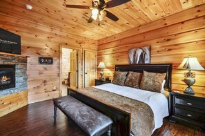 A cozy cabin-style bedroom with a large bed, wooden walls, a fireplace, and a ceiling fan. - Luxury 14br Haven Views Games Hot Tubs More (Sevierville)